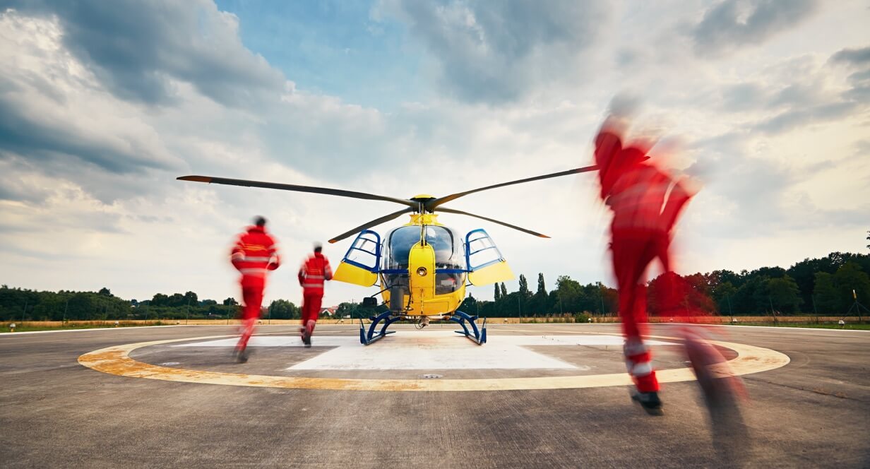 Menschen in orangefarbenen Uniformen rennen von dem Fotografen weg auf einen gelben Rettungshubschrauber zu.